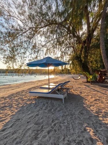 a beach with a blue umbrella and benches on the sand at Mafiya Resort in Koh Rong Island