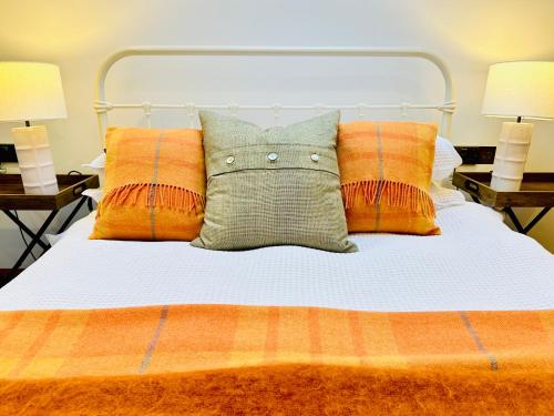 a bed with orange and white pillows and two lamps at Brora Escapes in Brora