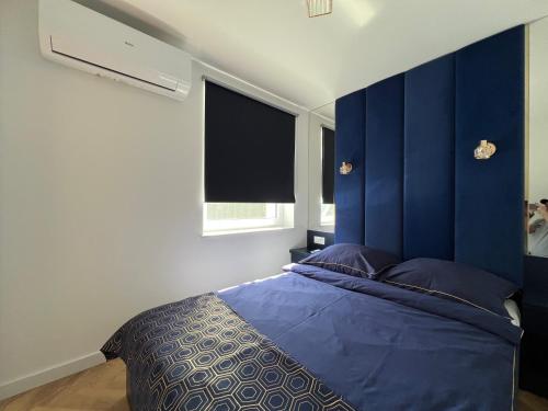a bedroom with a bed with a blue headboard and a window at Migor Apartamenty in Łeba