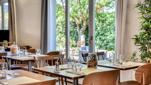 a restaurant with wooden tables and chairs and windows at Campanile NATURE - Besançon Ouest Chateaufarine in Besançon