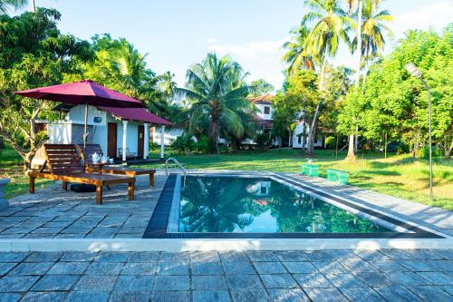 a swimming pool with a bench and an umbrella at Illukawela Walauwa in Embilipitiya