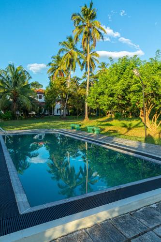 a swimming pool with palm trees in the background at Illukawela Walauwa in Embilipitiya