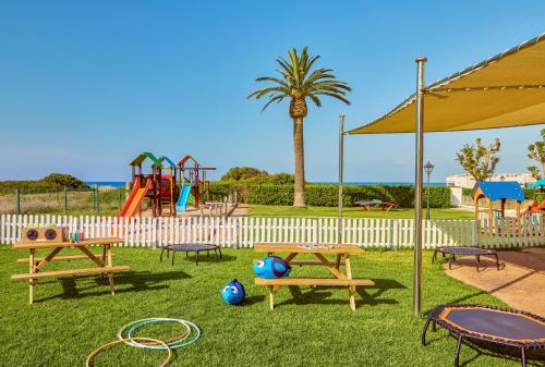a park with picnic tables and a playground with a palm tree at Sol Milanos Pingüinos in Son Bou