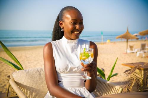 a woman sitting on the beach holding a drink at Kombo Beach Resort in Serekunda