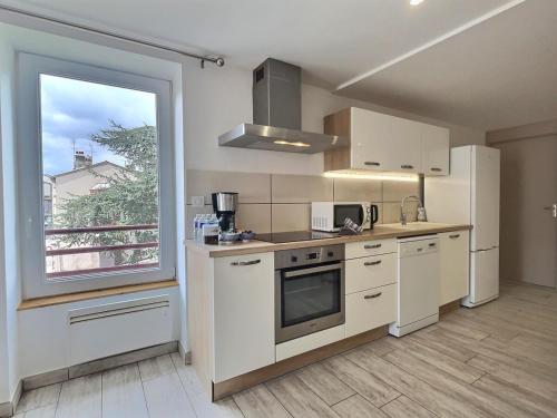 une cuisine avec des placards blancs et une grande fenêtre dans l'établissement L'Entre Deux Miss K Conciergerie, à Mâcon