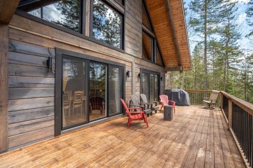 a large deck with red chairs on a house at L'Inukshuk - Chalet en bois ave Spa in Saint-Alexis-des-Monts