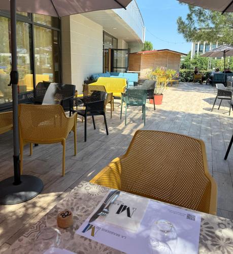 a patio with tables and chairs and a table with a menu at Le M & Spa Bordeaux Aéroport by Hôtels & Préférence in Mérignac