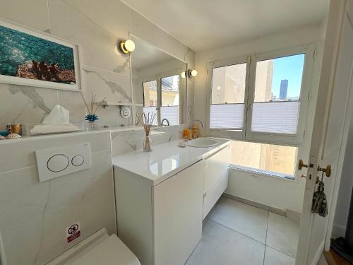 une salle de bain blanche avec un lavabo et une fenêtre dans l'établissement L'appartement Colombier, à Paris