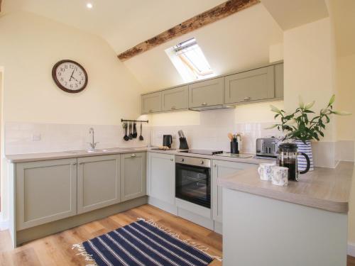 a kitchen with white cabinets and a clock on the wall at The Old Piggery in Shifnal