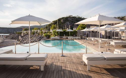 a swimming pool with white umbrellas and chairs and a swimming pool at Tivoli Portopiccolo Sistiana Apartments in Sistiana