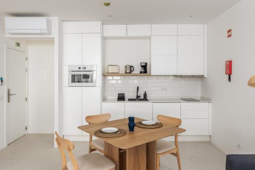 a kitchen with white cabinets and a wooden table and chairs at Estúdios Loreto - Fuseta in Fuzeta
