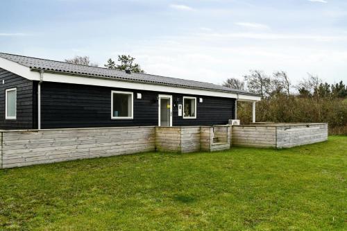 a black house with a fence in a yard at Black Wooden Summer House Near The Sea In Thy in Sønder Ydby