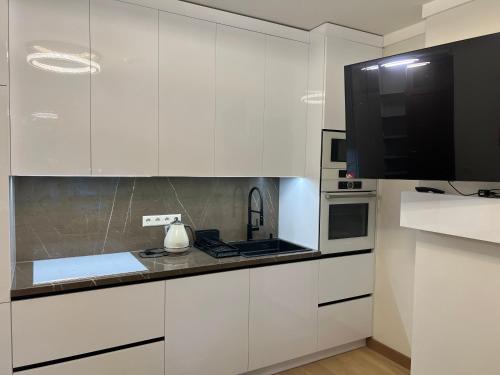 a kitchen with white cabinets and a flat screen tv at Nemuno Banga in Druskininkai