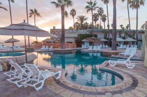 a pool with white chairs and an umbrella and palm trees at Estero Beach Hotel & Resort in Ensenada