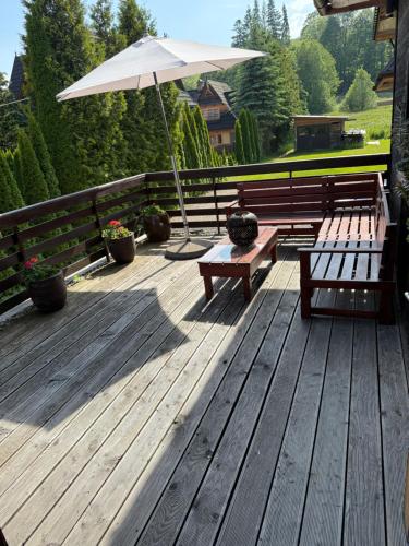 a wooden deck with two benches and an umbrella at Noclegi u Ewy in Witów