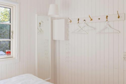 a bedroom with white walls and a window and hangers at Cottage Life In Intimate Wooden Cabin in Dronningmølle
