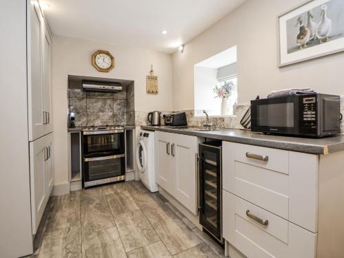 a kitchen with white cabinets and a microwave at Sunbird Cottage in Biddulph
