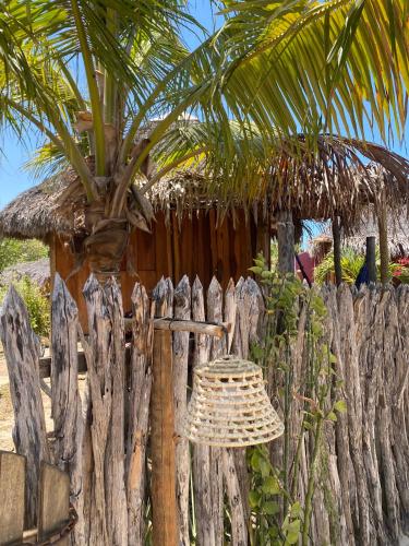 a straw hat on a wooden fence with a palm tree at Caju Bangalôs in Ponta do Anel