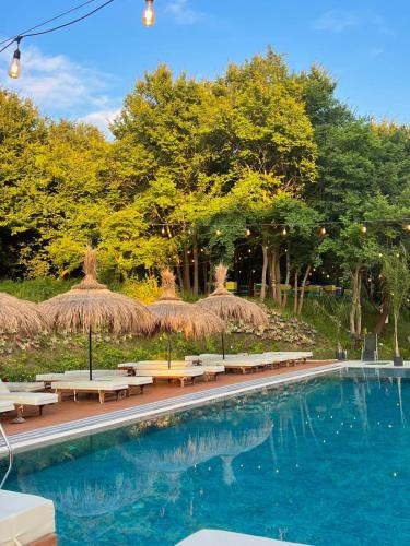 a swimming pool with tables and straw umbrellas and chairs at Olivia's Hill Resort in Durrës