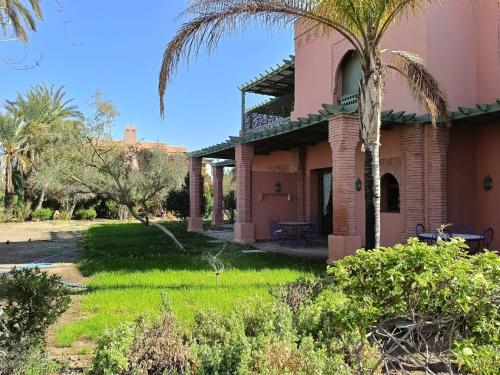 a pink house with a palm tree in the yard at Appartement standing piscine la palmeraie in Marrakech