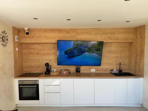 a kitchen with white cabinets and a tv on a wall at Apartmani Avanti Becici in Becici