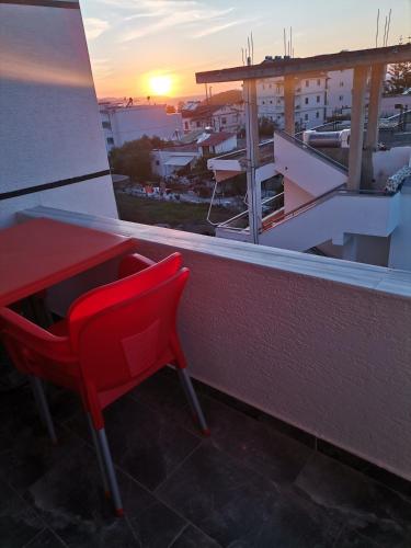 a red table and chairs on a balcony with the sunset at Koli Apartments in Ksamil