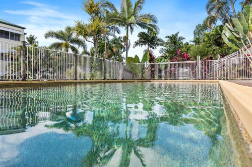 a swimming pool with a fence and palm trees at Palm & Sea Trinity Beach in Trinity Beach
