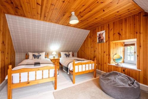 two beds in a room with wooden walls at Traditional Highland Cottage Near Loch Ness in Drumnadrochit