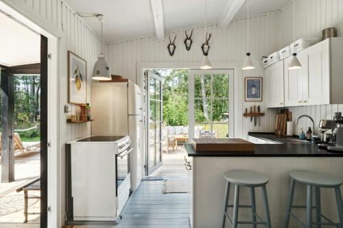 a kitchen with white cabinets and a counter with stools at Cozy Summerhouse On Bornholm in Vester Sømarken