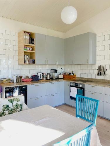 a kitchen with white cabinets and a table with a blue chair at Modern Glass House With A View Over Lake Lejondal in Bro