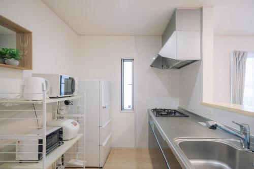 a white kitchen with a sink and a microwave at Comfort Miyabi-1号棟- in Yomitan
