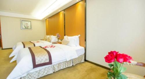 a bedroom with two beds and a vase with red flowers at Auspicious Hotel in Zhongshan
