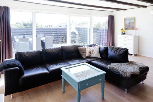 a black leather couch in a living room with a table at Atmosphere Close To Water Surrounded By Pines in Hvide Sande