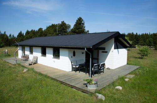 eine weiße Hütte mit einem Holzdeck auf einem Feld in der Unterkunft Dune House Near Bulbjerg in Frøstrup
