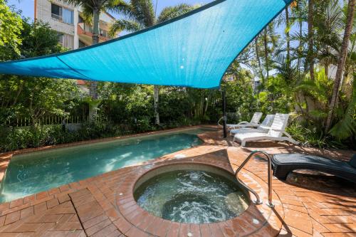 a swimming pool with a blue umbrella and chairs at Kings Row Apartments in Caloundra