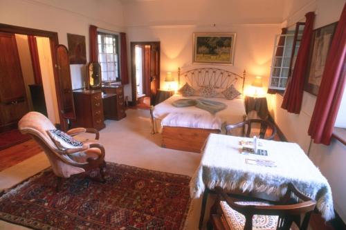 a bedroom with a bed and a table and chairs at Lekkerwijn Historic Country House in Simondium