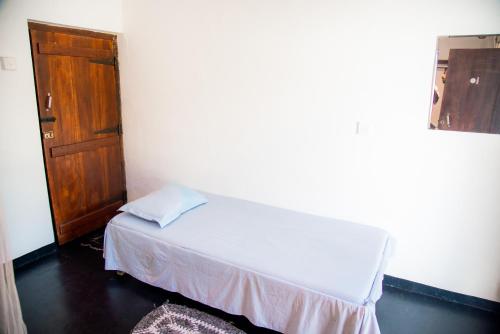 a small bedroom with a bed and a wooden door at Bay Dreams Beach Hotel & Surf Camp in Arugam Bay