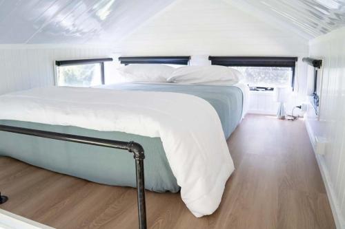 a bedroom with a large white bed with a wooden floor at Hill Creek Tiny House 1 by Tiny Away in Perwillowen