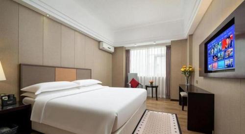 a bedroom with a large white bed and a flat screen tv at Zhuhai Aqueen Hotel in Zhuhai