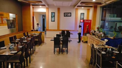 a restaurant with tables and chairs and people standing at a counter at Alps Residency - A Bergamont Hotel, Krishnagiri in Krishnagiri