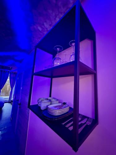 a black shelf with plates and glasses in a purple room at Capsule Nuage Jacuzzi Sauna in Fontaine-lʼÉvêque
