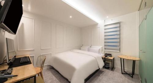 a white bedroom with a bed and a desk and a computer at Crossing Hotel in Seoul