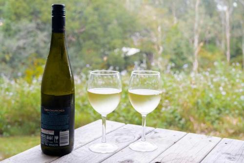 two glasses of white wine sitting on a wooden table at Hill Creek Tiny House 3 by Tiny Away in Perwillowen