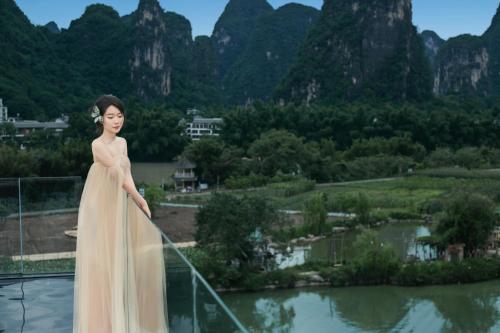 a woman in a dress standing on a balcony with mountains at Yangshuo Hidden Dragon Villa in Yangshuo