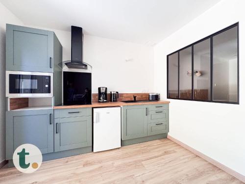 La cuisine est équipée de placards bleus et d'un réfrigérateur blanc. dans l'établissement Tranquiloue - Appart Centre-Ville - Puy du Fou 20min, aux Herbiers