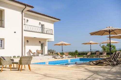 a villa with a swimming pool with chairs and umbrellas at Vila sa bazenom Vrnjačka Idila in Vrnjačka Banja