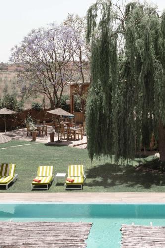two chairs and a table and a tree next to a pool at Jnan Lotf Marrakech - Le Jardin de la Bienveillance in Marrakech