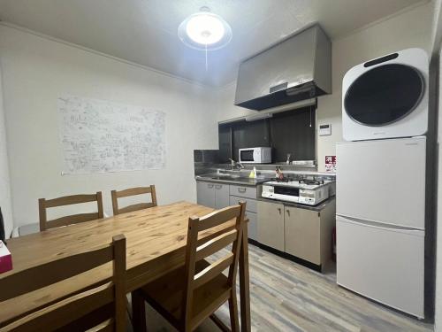 a kitchen with a wooden table and a white refrigerator at YadoPAP Ina town 宿ぱっぷ伊奈町 in Ina