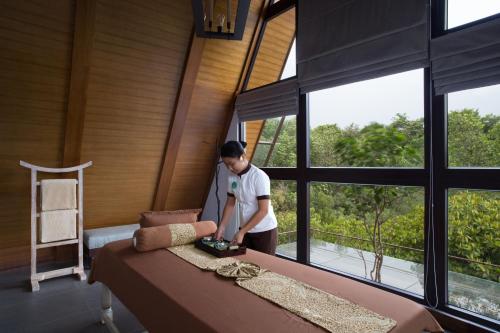 a man standing next to a bed in a room with windows at Plataran Menjangan Resort and Spa - CHSE Certified in Banyuwedang