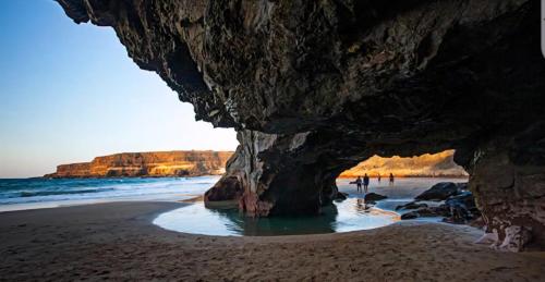 a cave on a beach with people in the water at Casa Dayaday in Puerto del Rosario